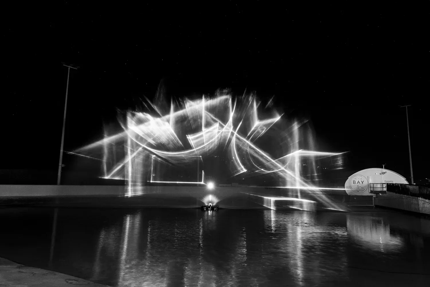 Lignes laser blanches au-dessus du lac, avec les bâtiments d’Alaïa Bay à droite