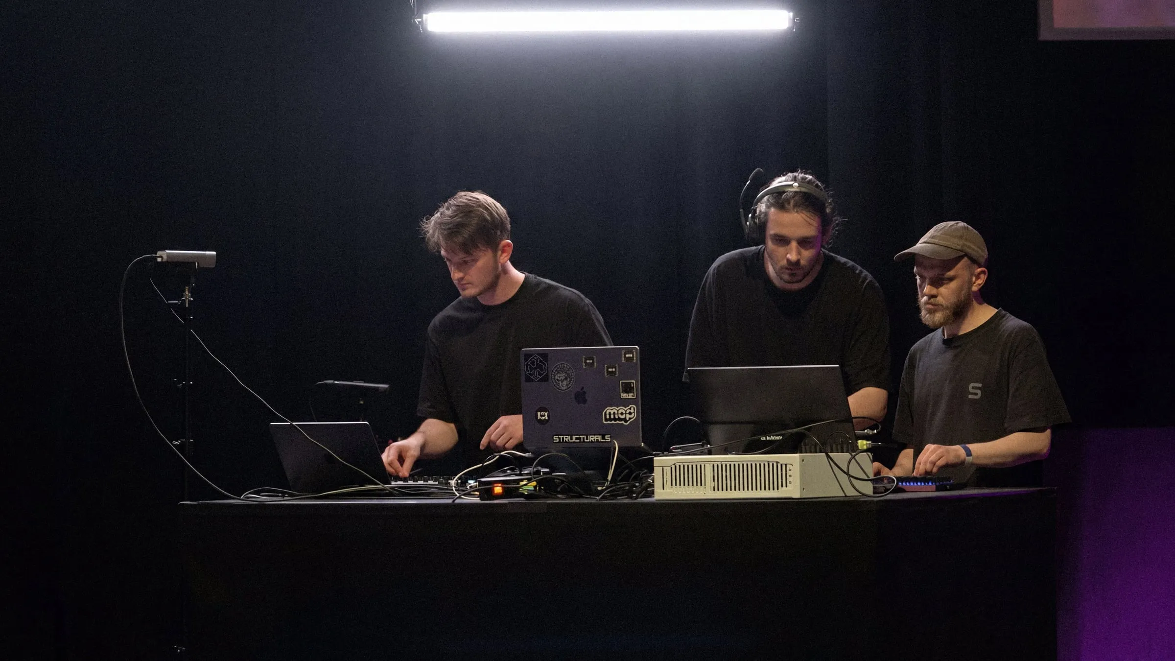 Les trois performeurs aux machines sur scène, sous une barre lumineuse